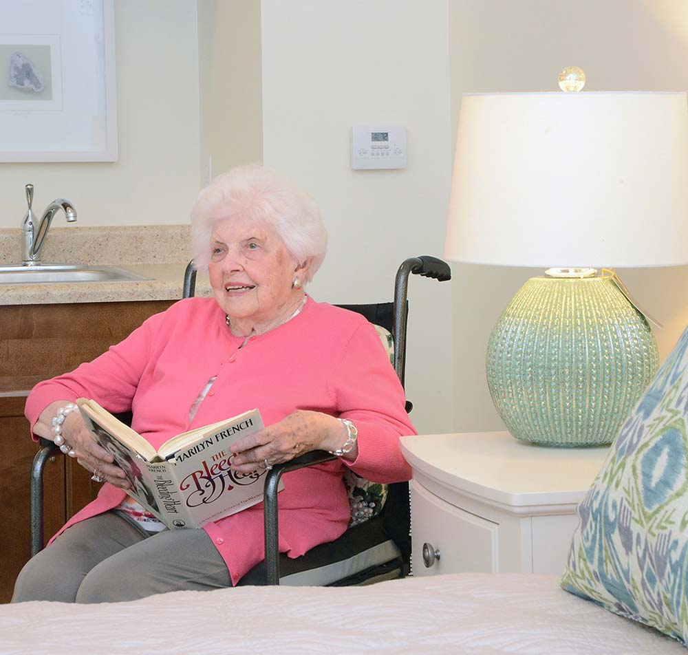 woman reading a book sits next to a bed