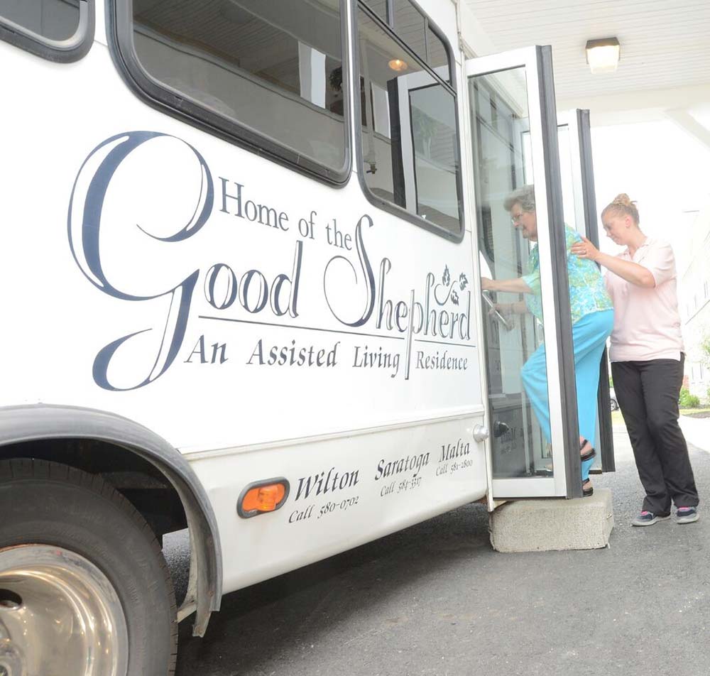 home of the good shpherd bus while residents being helped on by an assistant