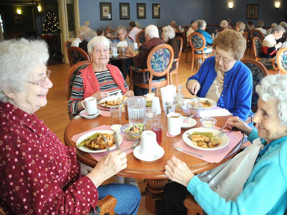 resident sit at a table eating food showing the dining room and types of food