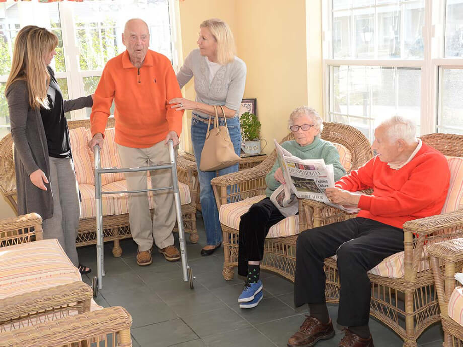 residents sit and share a newspaper while another resident is visited by family